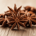 Primer plano fotorrealista de varias vainas enteras y secas de anís estrellado (Illicium verum) dispuestas artísticamente sobre una superficie de madera rústica. La intrincada forma de estrella y el color marrón cálido deben ser resaltados por una luz suave y natural, enfatizando su naturaleza aromática y visualmente atractiva.